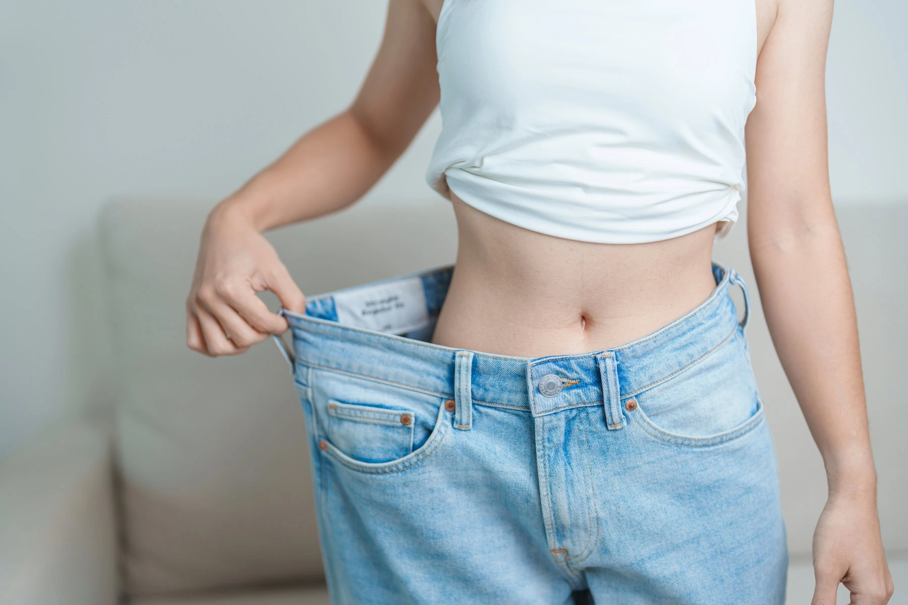 Person demonstrating weight loss by holding out loose jeans